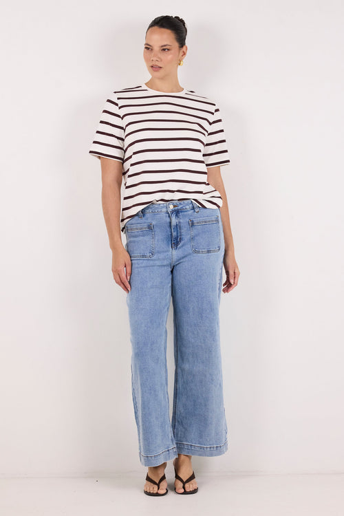 A woman modeling a short-sleeve black and white horizontally striped t-shirt paired with light-wash wide-leg blue jeans and black sandals, standing against a plain white studio background.