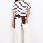 Woman wearing a black and white striped shirt with white pants on a white background