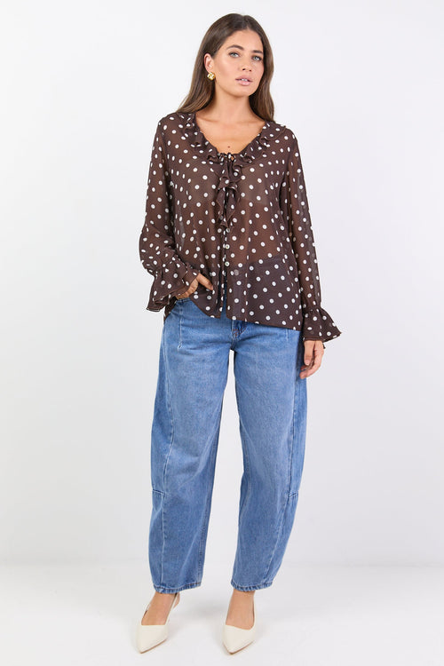 Woman wearing a brown polka dot blouse and blue jeans on a white background
