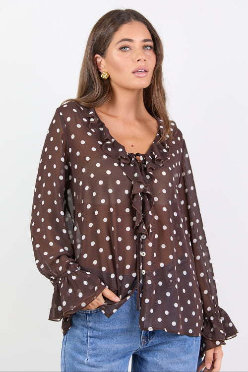 Woman wearing a brown polka dot blouse with blue jeans on a white background