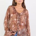 Woman wearing a brown floral blouse with blue jeans on a white background