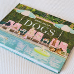 The book 'Dogs' by Gray Malin, featuring a colorful cover illustration of dogs relaxing by a pool, resting on a white textured fabric surface.