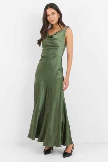 A woman modeling a sleeveless olive green satin maxi dress with a cowl neckline and a flared skirt, standing against a plain white studio background.