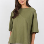 A woman modeling an oversized olive green short-sleeve top and off-white wide-leg pants against a clean white studio background.