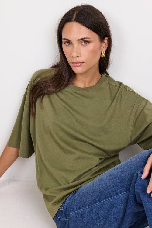 Woman wearing an olive green t-shirt and blue jeans sitting on a white floor.