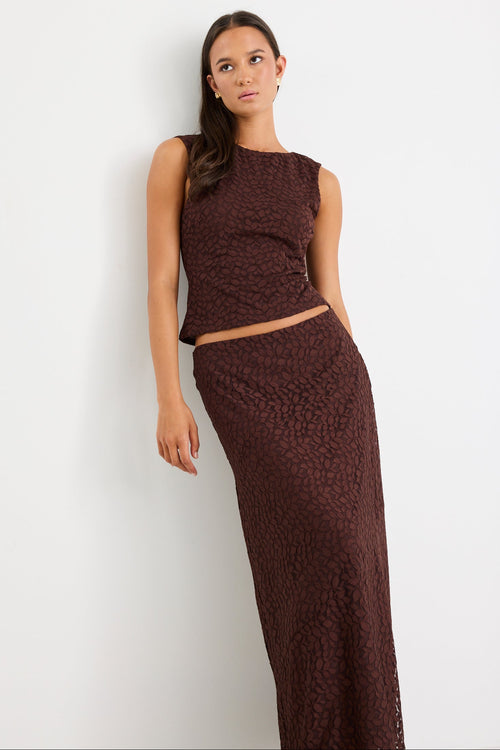 Woman wearing a brown sleeveless top and long skirt against a white background