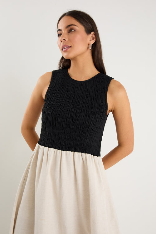 Woman wearing a black sleeveless top and beige skirt against a plain background