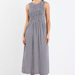 Woman wearing a navy mini gingham midi dress with a shirred bodice, sleeveless crew neckline, and relaxed gathered skirt.