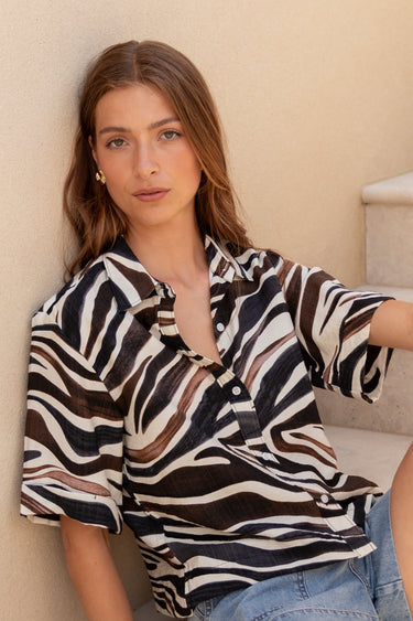 Woman sitting on a staircase wearing a zebra-striped shirt and denim shorts.