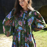Woman wearing a floral dress standing outdoors with a dark background