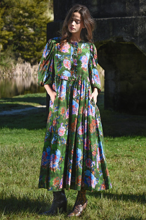 Woman wearing a floral dress standing outdoors near a body of water.