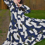 Woman wearing a long, patterned dress outdoors with a rustic building in the background