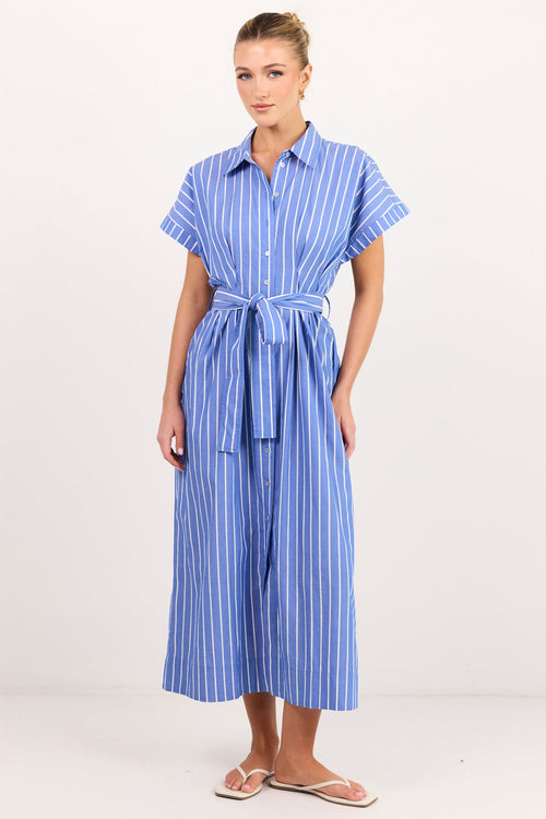 A woman modeling a blue and white vertically striped short-sleeve jumpsuit with a matching tie belt, standing against a plain white studio background.