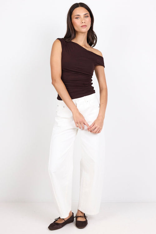 A woman modeling a dark brown off-the-shoulder ribbed top and white wide-leg pants against a plain white studio background.