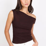A woman modeling a dark brown off-the-shoulder ruched top paired with white pants, set against a plain white studio background.