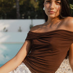Woman in a brown top sitting by a pool with greenery in the background