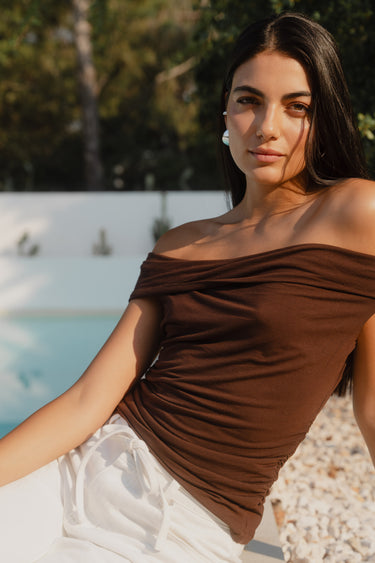 Woman in a brown top sitting by a pool with greenery in the background