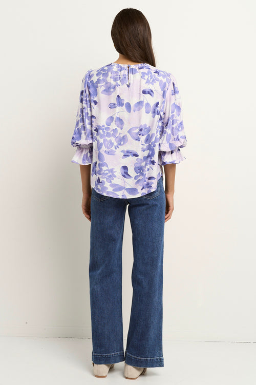 Model wears a white and blue floral blouse with dark blue jeans