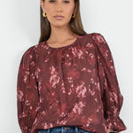 Woman wearing a burgundy floral blouse and blue jeans on a white background