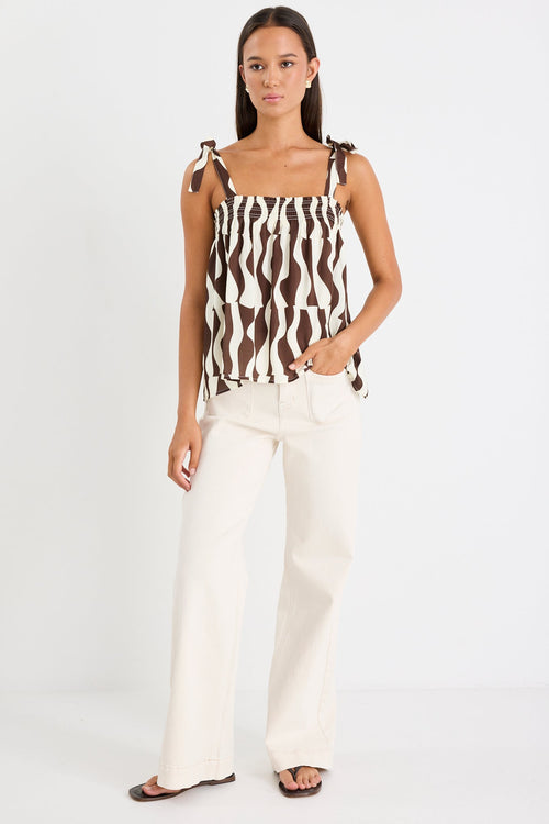 Woman wearing a brown and white geo print top and white jeans