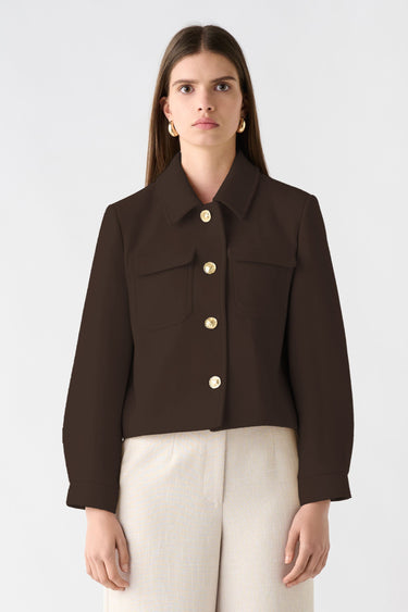 Woman wearing a brown jacket and beige pants on a white background