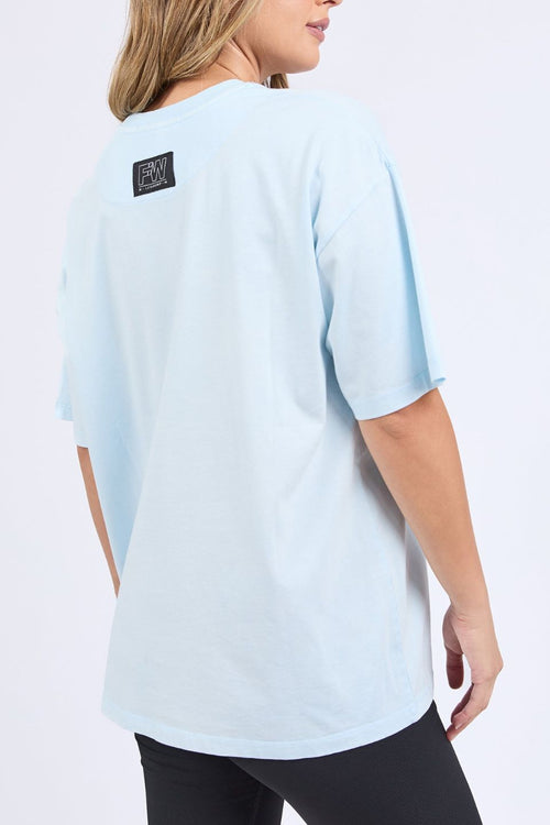 Woman wears an oversized pale blue t-shirt with short sleeves, a round neckline, and small 