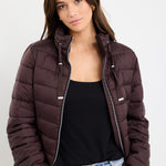 Woman wearing a brown puffer jacket over a black top and blue jeans on a white background