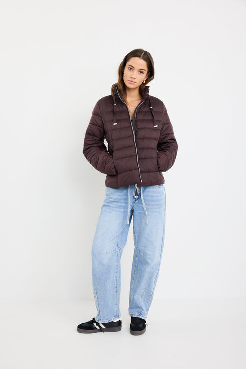 Person wearing a brown puffer jacket and light blue jeans on a white background