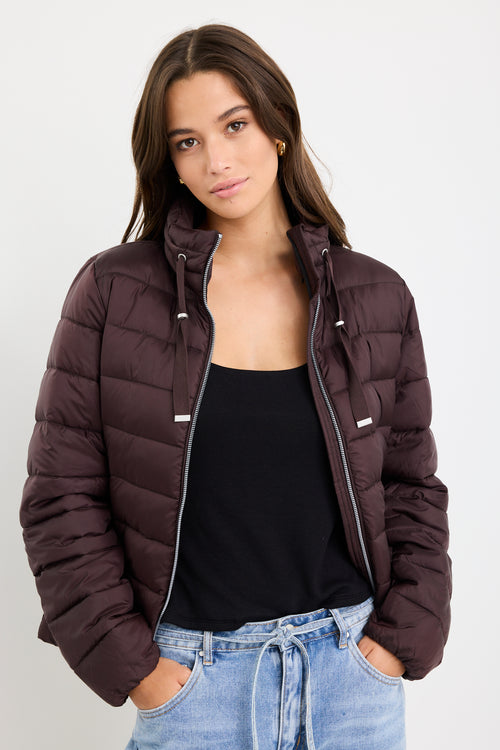 Woman wearing a brown puffer jacket over a black top and blue jeans on a white background