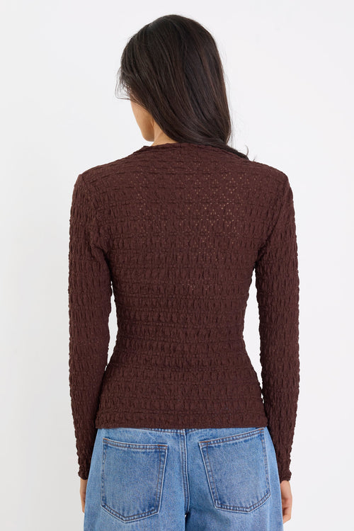 Person wearing a brown textured sweater and blue jeans on a white background