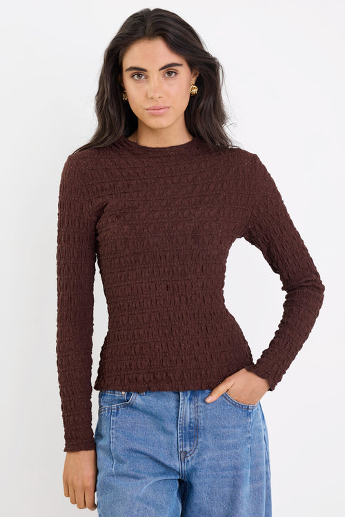 Woman wearing a brown ribbed sweater and blue jeans on a white background