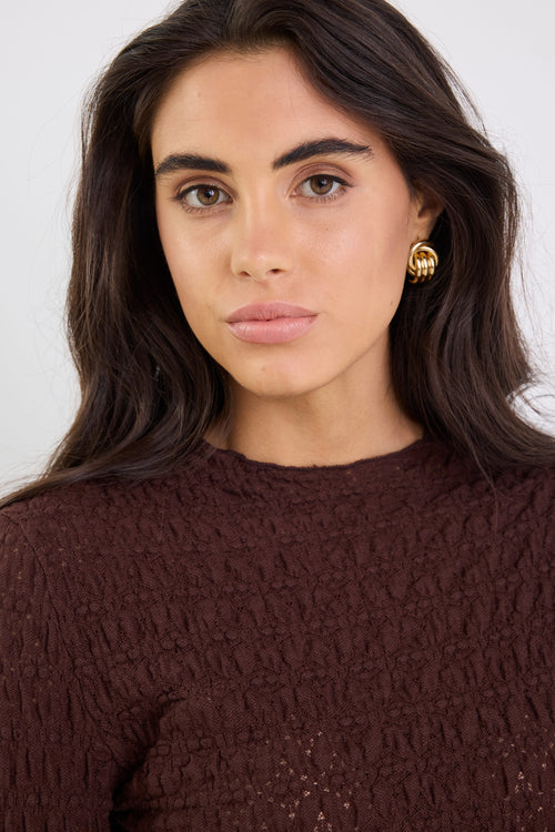 Woman wearing a brown textured sweater with a plain background