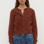 Woman wearing a brown cardigan and blue jeans against a white background