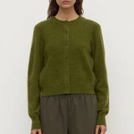 Person wearing a green cardigan and brown pants against a white background