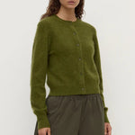 Woman wearing a green cardigan and brown pants on a white background