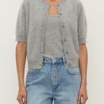 Person wearing a gray cardigan over a light blue top and jeans on a plain background