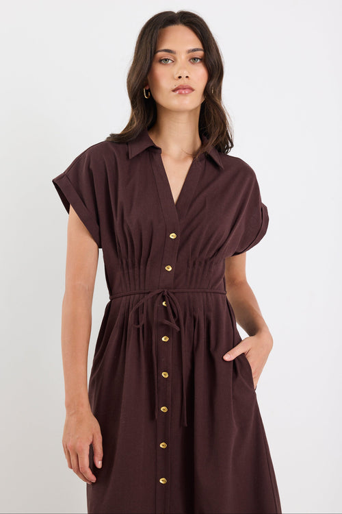 Woman wearing a brown dress with gold buttons on a white background