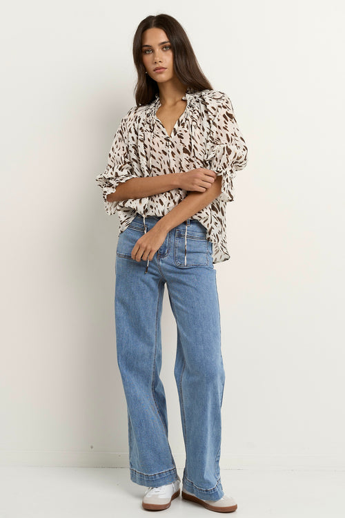 Woman wearing a loose animal-print blouse with ruffled collar and blue wide-leg jeans.