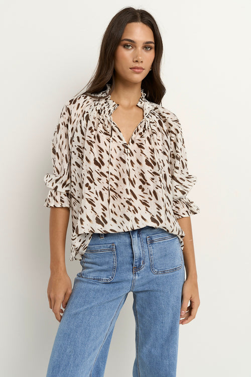 Woman wearing a loose animal-print blouse with ruffled collar and blue wide-leg jeans.