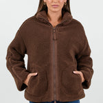 Woman wearing a chocolate brown sherpa fleece zip jacket and blue jean against a white background