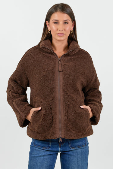 Woman wearing a chocolate brown sherpa fleece zip jacket and blue jean against a white background