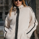 Woman wearing a white fleece jacket with black zipper and trim, standing outdoors.