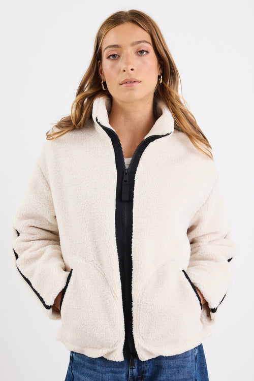 Woman wearing a cream puffer jacket with black zipper on a white background