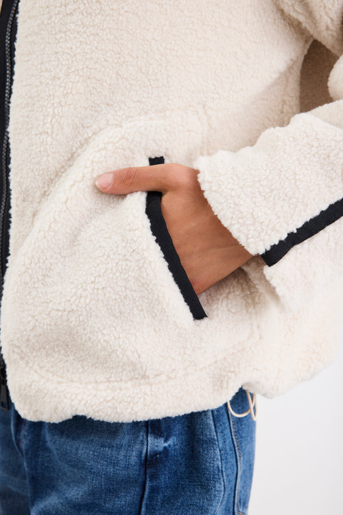 Close-up of a person wearing a white fleece jacket with black trim, holding their hand in front.