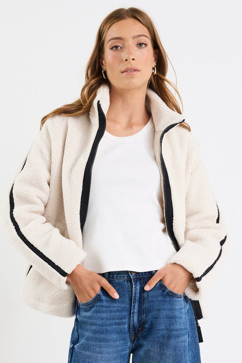 Person wearing a white jacket, white shirt, blue jeans, and white sneakers on a white background