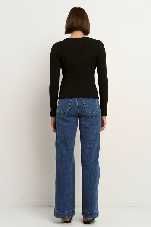 Woman wearing a fitted black ribbed button-down cardigan with a deep V neckline and blue jeans.