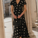 Woman in a black polka dot dress standing between classical columns.