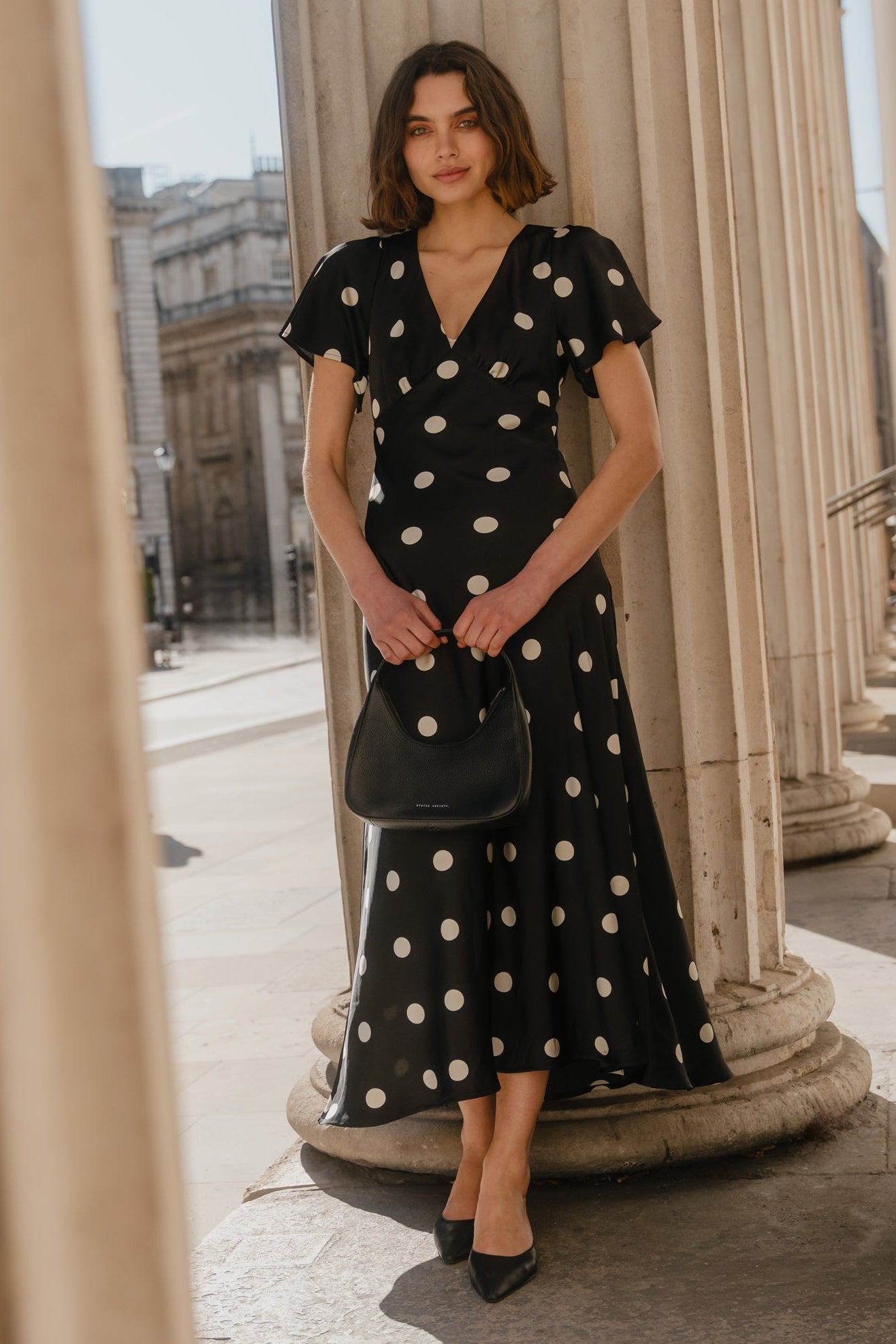 Woman in a black polka dot dress standing between classical columns.
