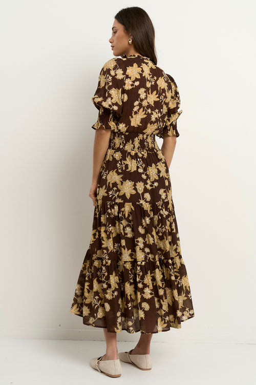 Woman wearing a brown floral midi dress with puff sleeves, a shirred waist, and a tiered skirt.