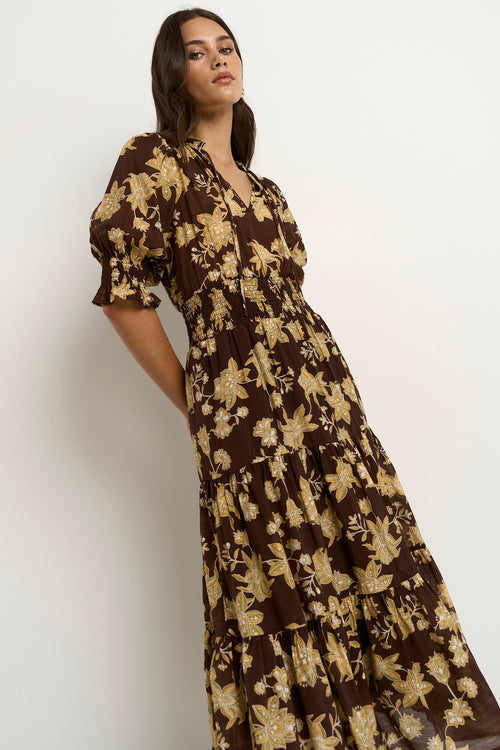 Woman wearing a brown floral midi dress with puff sleeves, a shirred waist, and a tiered skirt.